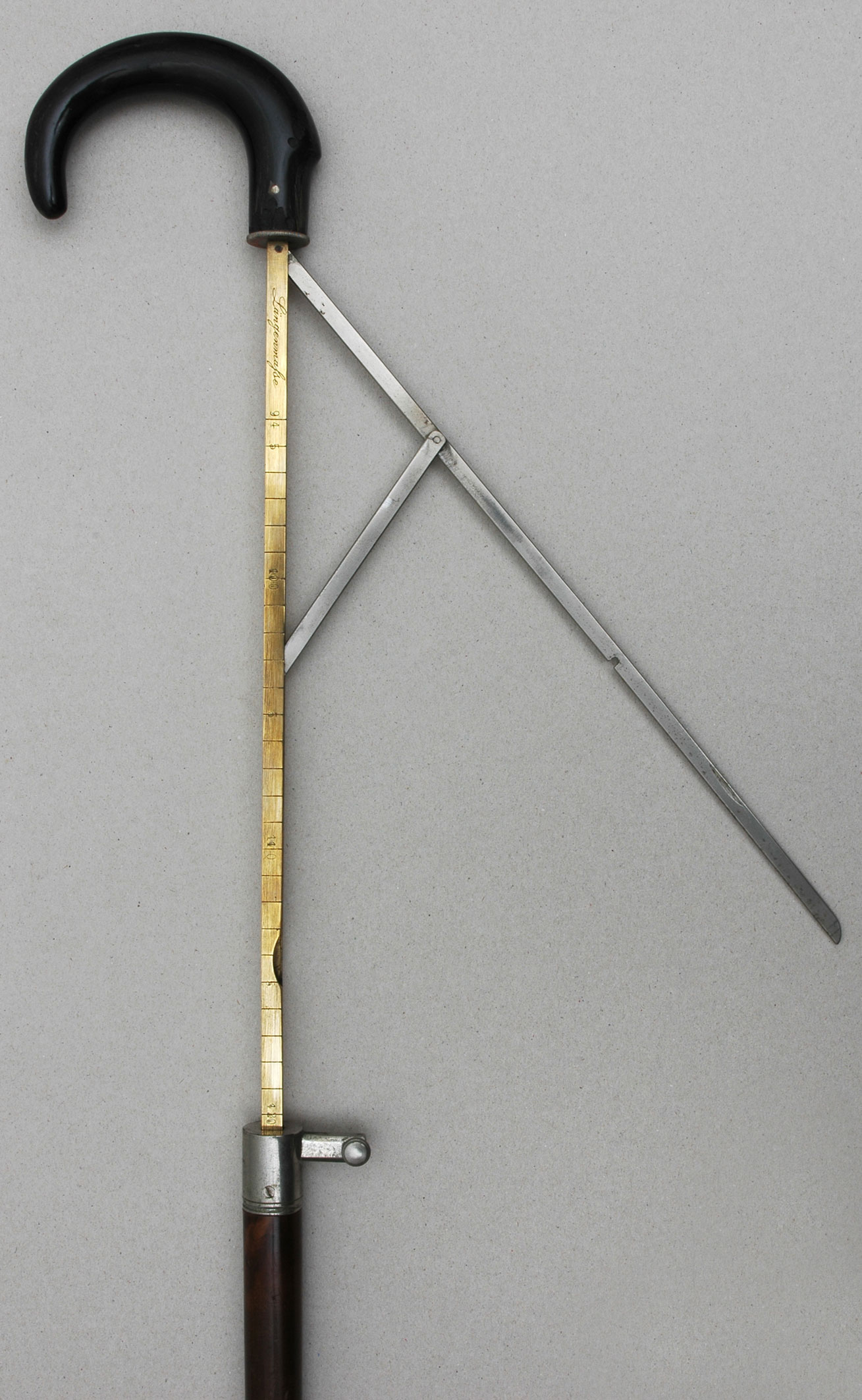 Przedmiot przedstawiony na zdjęciu to najprawdopodobniej laska pomocna przy chodzeniu, lub laska przeznaczona do parasola. Ma czarną rączkę wywiniętą w łagodny łuk, oraz pręt w kolorze złotym do którego przylega drewniana nóżka.