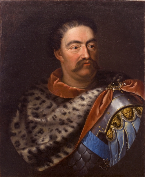 Portret olejny. Król Jan III Sobieski ubrany w antykizowaną zbroję i płaszcz lampraci spiety broszą z kamieniem. Patrzy w prawą stronę. 