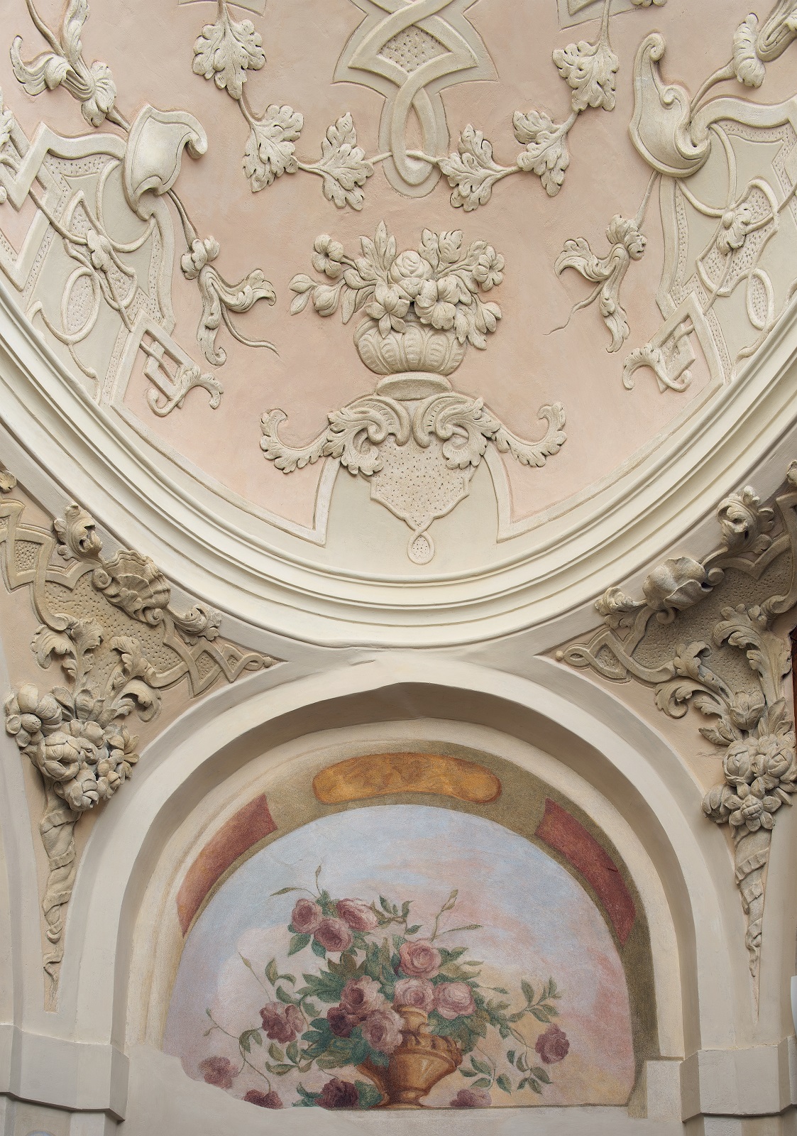 Kolorowe zdjęcie fragmentu ozdób pałacowych. Przedstawia kosz z kolorowymi kwiatami, a powyżej sztukaterie z motywami kwiatowymi. Jest to klatka schodowa przy Sali Uczt Jana III w pałacu wilanowskim.