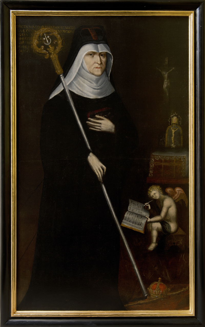 Portret olejny oprawiony w złoto-czarną ramę. Przedstawia zakonnicę we wnętrzu. Po prawej stronie postaci, na małym krześle, siedzi anioł, który pisze piórem w księdze. Pod nim leży korona królewska. Powyżej stół, a nad nim krzyż. Jest to portret benedyktynki Doroty Magdaleny Daniłowiczówny.