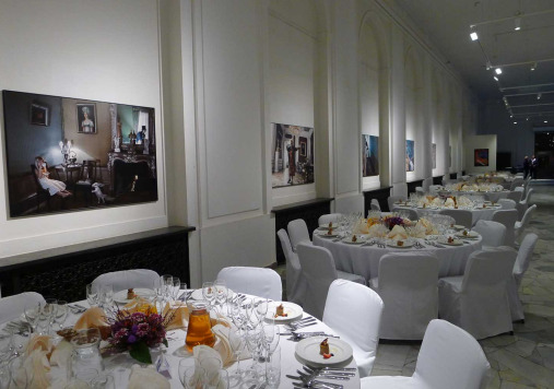 Kolorowe zdjęcie przedstawia wnętrze, gdzie ustawione są okrągłe stoły wraz z krzesłami. Jest to miejsce do organizacji uroczystych przyjęć.