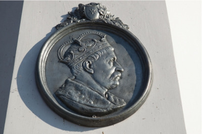 Zdjęcie współczesne. Przedstawia medalion z popiersiem króla Jana III. Król ujęty z profilu, patrzy w prawo. Na głowie ma koronę królewską. Medalion umieszczony jest na pomniku Jana III Sobieskiego w Cieszanowie. 