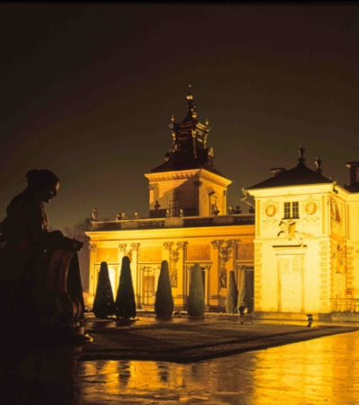 Współczesna kolorowa fotografia. Przedstawia fragment zabudowań pałacu w Wilanowie. Widzimy oświetloną na żółto architekturę.