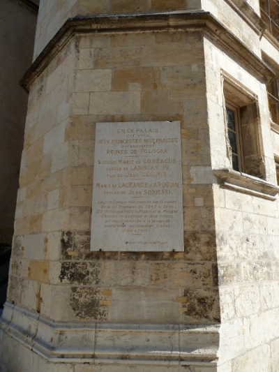 Zdjęcie współczesne. Przedstawia płytę zamontowaną na kamiennej ścianie starego budynku pałacowego. Na płycie napis w języku francuskim. Jest to tablica pamiatkowa w Palais Ducal. 
