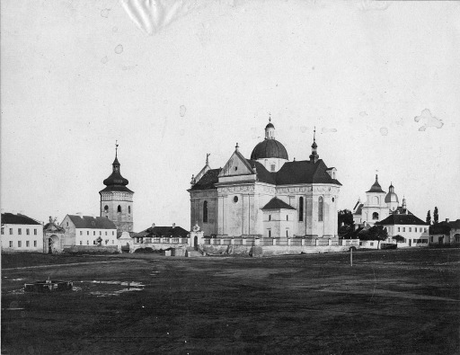 Stara, czarno-biała fotografia. Przedstawia  zabudowania klasztorne na tle pejzażu. 