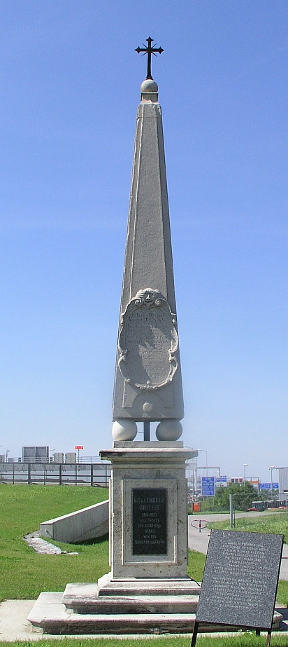 Kolorowe zdjęcie wykonane w plenerze. Przedstawia obelisk w Schwechat, który powstał, by upamiętnić miejsce spotkania cesarza Leopolda I z królem Janem III, dnia 15 września 1683 roku.