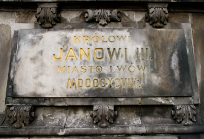 Fotografia kolorowa. Zbliżenie na pomnik konny króla Jana III w Gdańsku. Przedstawia zbliżenie na fragment płaskorzeźby na której widniej napis: „Królowi Janowi III. Miasto Lwów”.