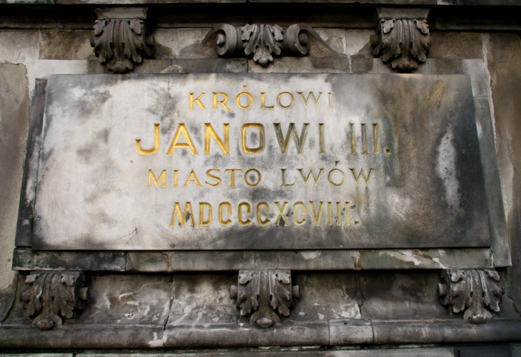 Fotografia kolorowa. Zbliżenie na pomnik konny króla Jana III w Gdańsku. Przedstawia zbliżenie na fragment płaskorzeźby na której widniej napis: „Królowi Janowi III. Miasto Lwów”.