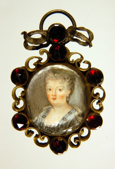
Portret Teresy Kunegundy Sobieskiej. Jest to miniatura oprawiona w srebro i czerwone kamienie. Przedstawia popiersie kobiety w średnim wieku, która patrzy na wprost. Ubrana jest w srebrną suknię z kolczykami w uszach. Fryzura upięta do tyłu.