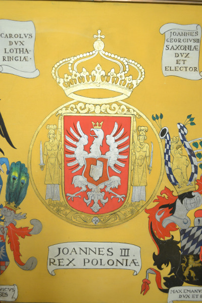 Zdjęcie przedstawia fragment fresu. Jest to herb Polski z orłem białym w koronie podtrzymywany prez dwie kobiety w szatach antycznych z mieczami. Nad godłem złota korona oparta o złotą obręcz. POd godłem napis: Joannes III REX POLONIAE. 