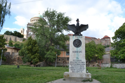 Zdjęcie przedstawia pomnik Jana III Soebieskiego w Ostrzyhomiu. Pomnik składa się z wysokiego, kamiennego cokołu z płaskorzeźbą - portretem króla Jana III Sobieskiego. Na szczycie znajduje się rzeźba orła w koronie z rozłożonymi skrzydłami. 