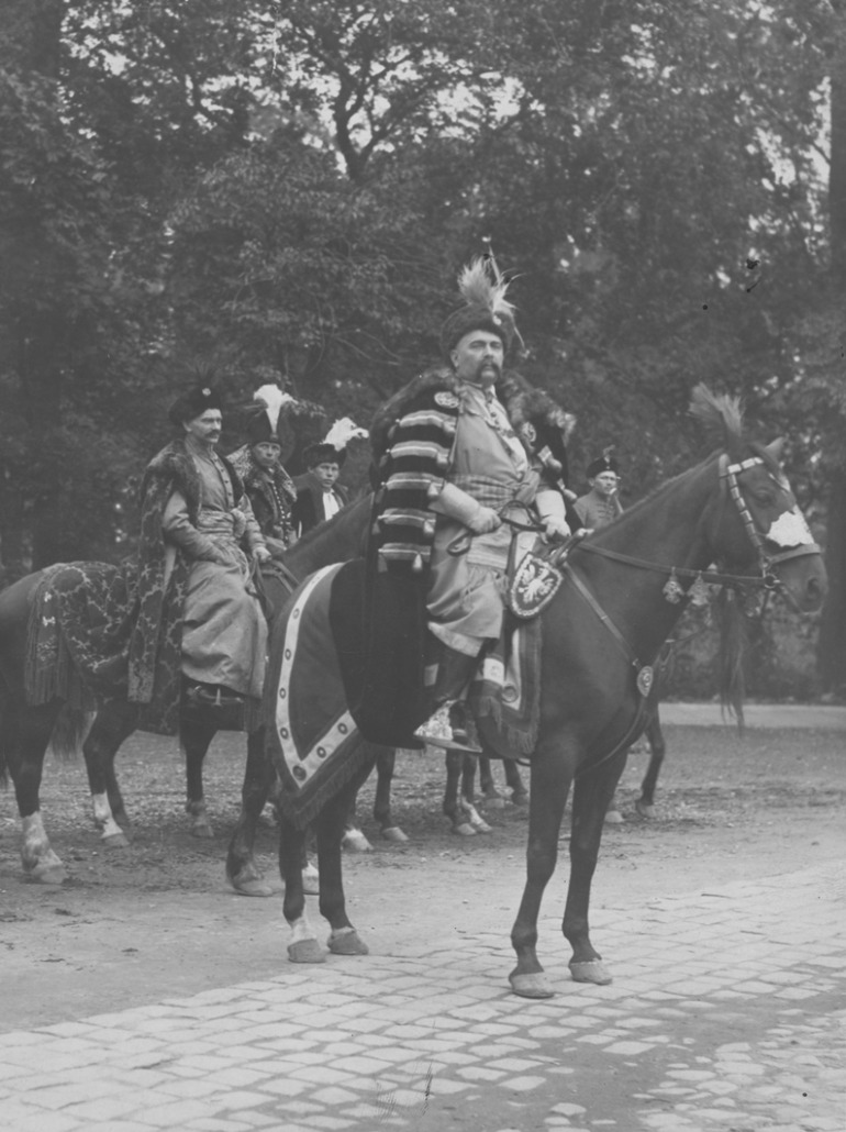 Zdjęcie czarno-białe. Dokumentuje rocznicę odsieczy wiedeńskiej i uroczystości w Warszawie. Uczestnicy parady w strojach historycznych stoją przed pomnikiem króla Jana III Sobieskiego w Łazienkach Królewskich. 
