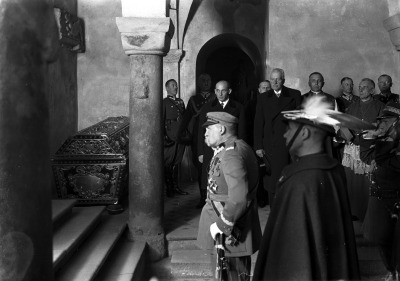 Czarno-białe zdjęcie archiwalne. Dokumentuje złożenie hołdu w krypcie króla Jana III Sobieskiego na Wawelu. Na zdjęciu widoczni są m.in.: marszałek Józef Piłsudski (na pierwszym planie z lewej), płk Witold Wartha (na pierwszym planie, bokiem), dalej, od lewej: płk Adam Sokołowski, płk Jan Głogowski, premier Janusz Jędrzejewicz, Bronisław Hełczyński, prezydent Ignacy Mościcki, bp polowy Józef Gawlina, gen. Aleksander Narbut-Łuczyński, abp Adam Sapieha. Jest to zdjęcie wykonane z okazji 250 rocznica Odsieczy Wiedeńskiej - Święto Kawalerii w Krakowie.
