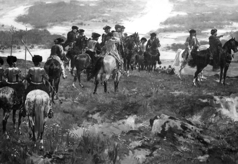 Zbliżenie na obraz „Jan III Sobieski pod Wiedniem”. Jest to olej na płótnie. Przedstawia scenę historyczną. Na pagórku stoją jeźdźcy na koniach. Zatrzymali się i patrzą na roztaczające się przed nimi miasto. 