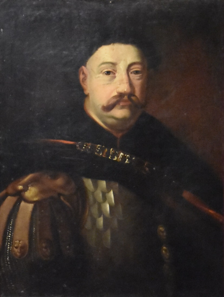 Portret Jana III Sobieskiego w zbroi i ciemnym płaszczu narzuconym na ramiona. Jest to olej na płótnie. Król patrzy dumnie na wprost. Tło obrazu ciemne.