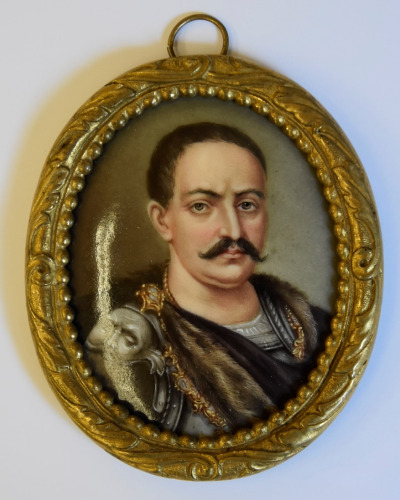 Miniatura portretowa Jana Sobieskiego wykonana farbami olejnymi na porcelanie. Portret oprawiony  w złotą, dekoracyjną ramkę. Przedstawienie króla w zbroi i płaszczu na ramionach. 
