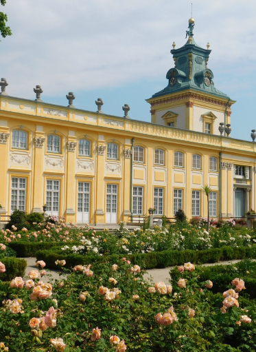 Kolorowe zdjęcie współczesne. Przedstawia widok na pałac w Wilanowie. Na pierwszym planie ogród różany.