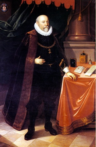 Barwna reprodukcja obrazu. Przedstawia portret mężczyzny we wnętrzu. Portretowany ubrany jest w ciemny strój i czarny płaszcz. Pod szyją ma biały kołnierz. Opiera swoją lewą rękę na stole pokrytym aksamitem, na którym leżą książki, listy i przedmioty. Mężczyzna stoi na tle kotary. W lewym górnym rogu znajduje się herb. Jest to portret Wilhelma z Rožemberku. 