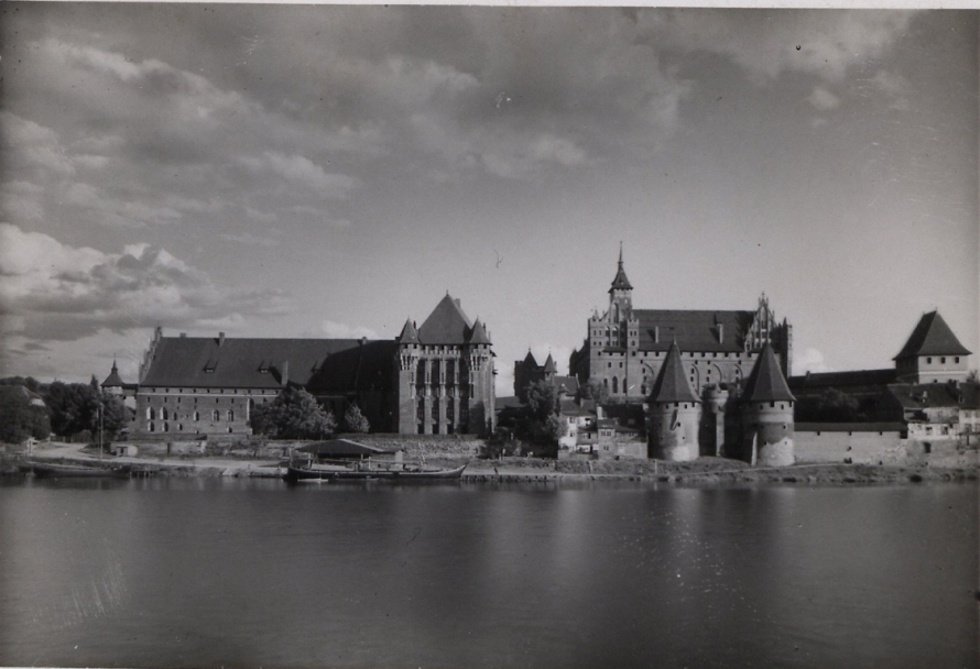 Czarno-białe zdjęcie archiwalne. Przedstawia zamek Malbork. Jest to widok Zamku Wysokiego i Pałacu Wielkich Mistrzów od strony zachodniej.