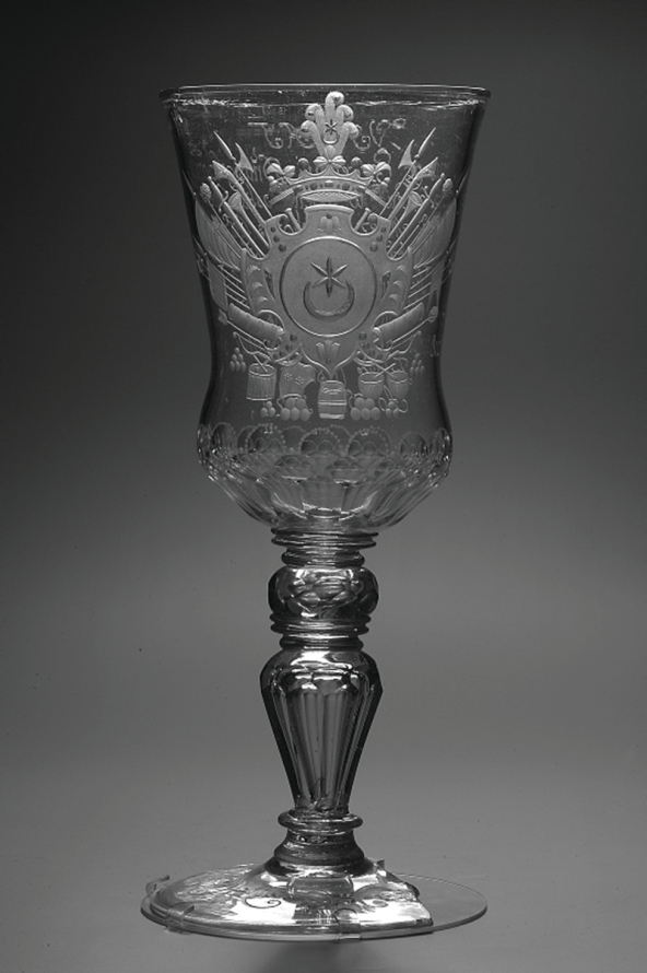 Wysoki kielich ze szkła z okrągłą podstawą i nóżką. Kielich z herbem „Leliwa” i napisem dedykacyjnym dla Adama Mikołaja Sieniawskiego, hetmana wielkiego koronnego, kasztelana krakowskiego. 