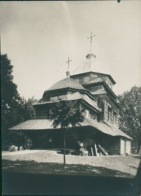 Czarno-białe zdjęcia archiwalne. Przedstawia widok na cerkiew. Jest to drewniana Cerkiew Zaśnięcia Bogurodzicy w Jaworowie. Zdjęcie pochodzi z około 1910 roku.