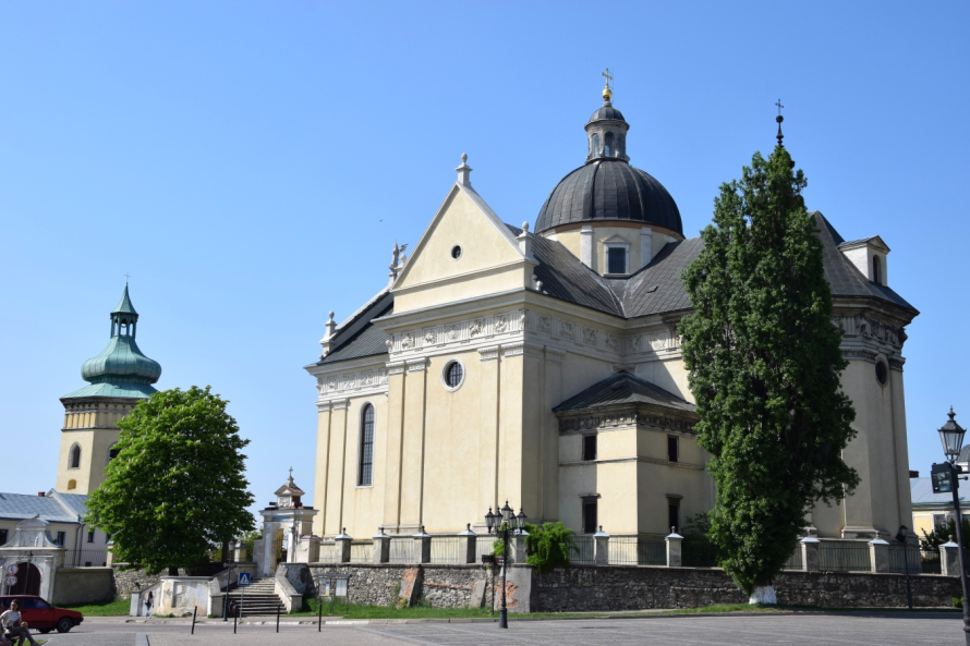 Kolorowa fotografia współczesna. Przedstawia widok na świątynię w stylu klasycyzującym z kopułą na środku. Jest to kościół parafialny w Żółkwi. 