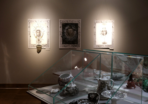 Wnętrze wystaw. Na ścianie 3 obrazy, na stole pod szklaną pokrywą znajdują się naczynia.