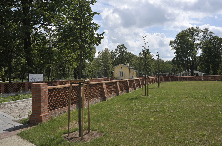 Przedpole pałacu z ceglanym murkiem i żółtym małym budynkiem w oddali.