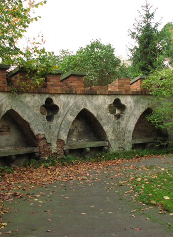 Niszczejąca brama z ostrołukowymi detalami architektonicznymi wśród drzew.