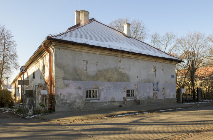 Podłużny beżowy budynek z obdrapanym tynkiem.