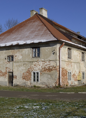 Podłużny beżowy budynek z obdrapanym tynkiem. Na dachu leży śnieg.